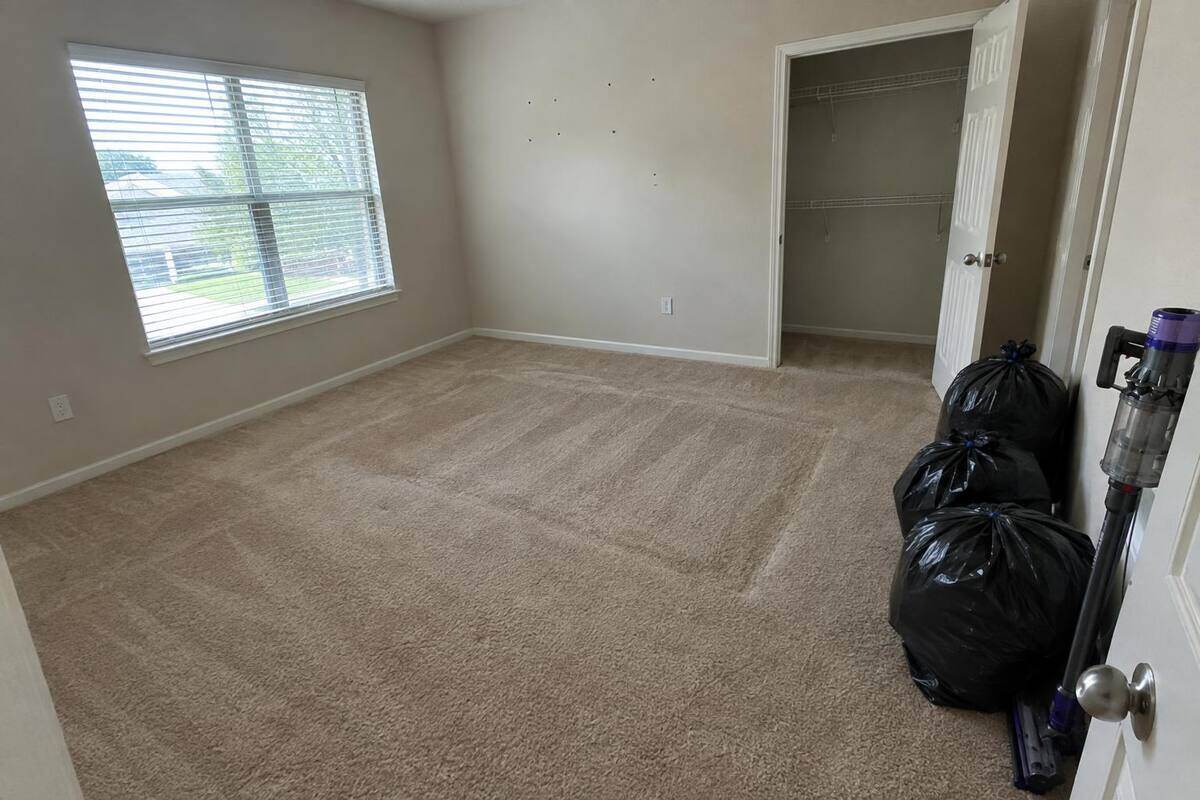 An emptied bedroom with vacuum lines in the carpet and three black bags by the door