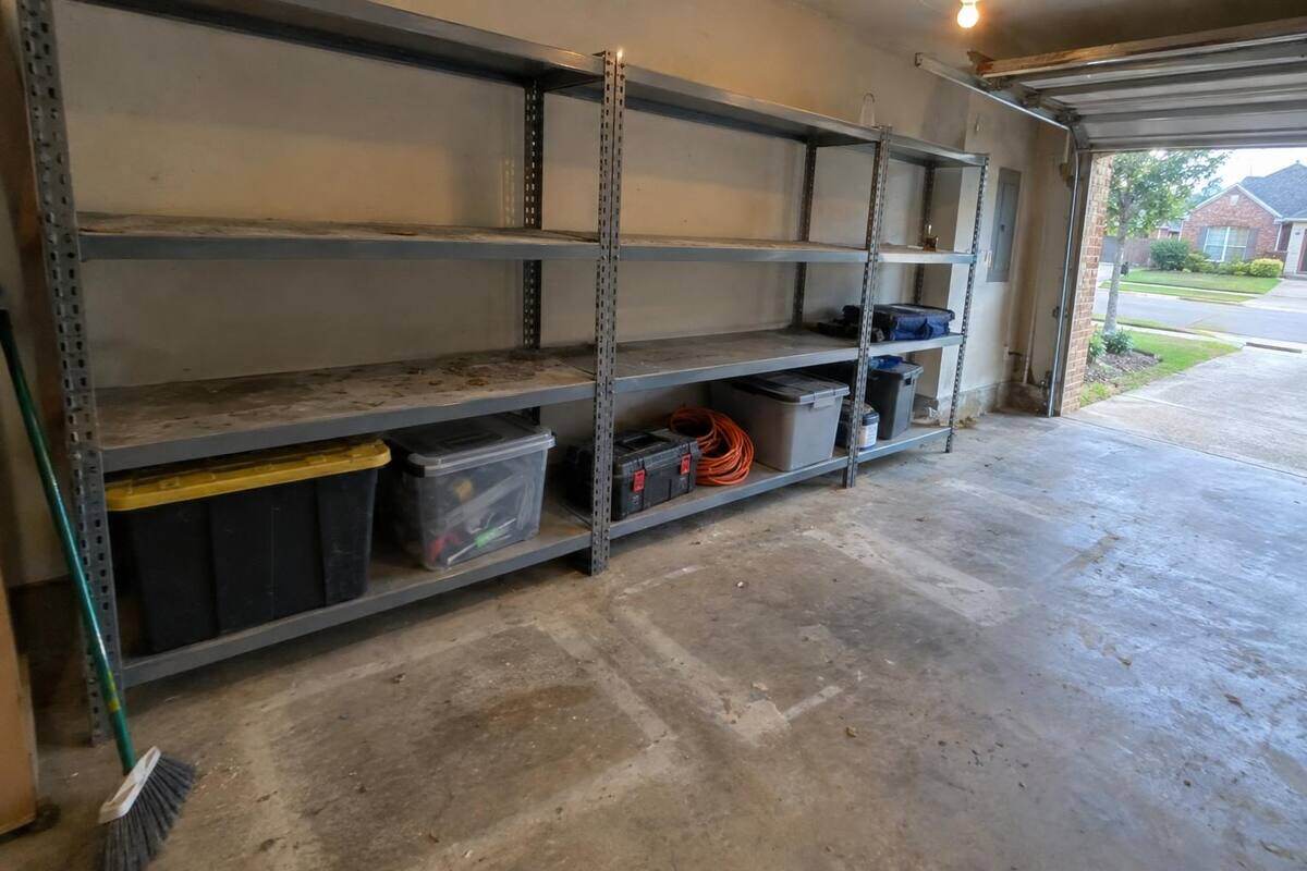 Metal garage shelving half emptied, bins and tools left on the lower shelves, bare concrete where boxes stood