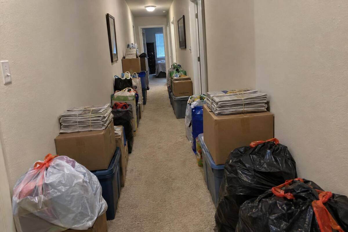 A hallway with boxes and bags stacked along both walls and a narrow path cleared down the middle
