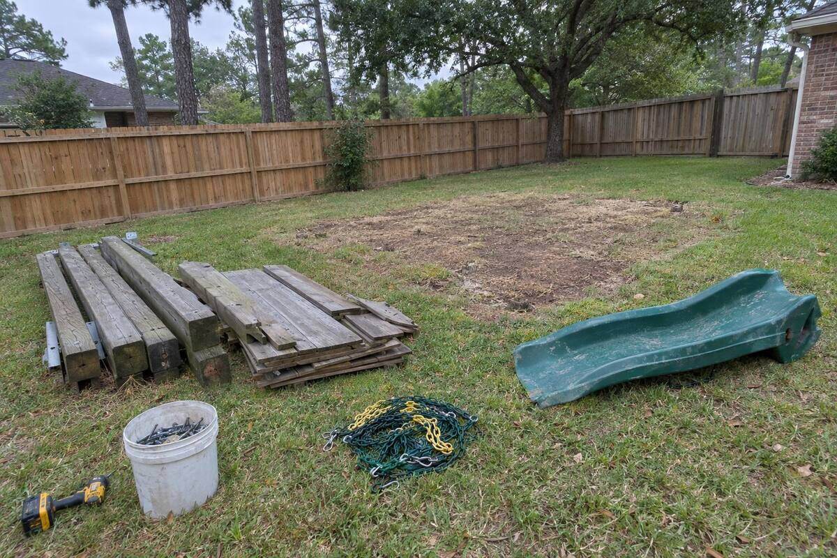 A wooden backyard playset taken apart into beams and a green plastic slide stacked on the grass