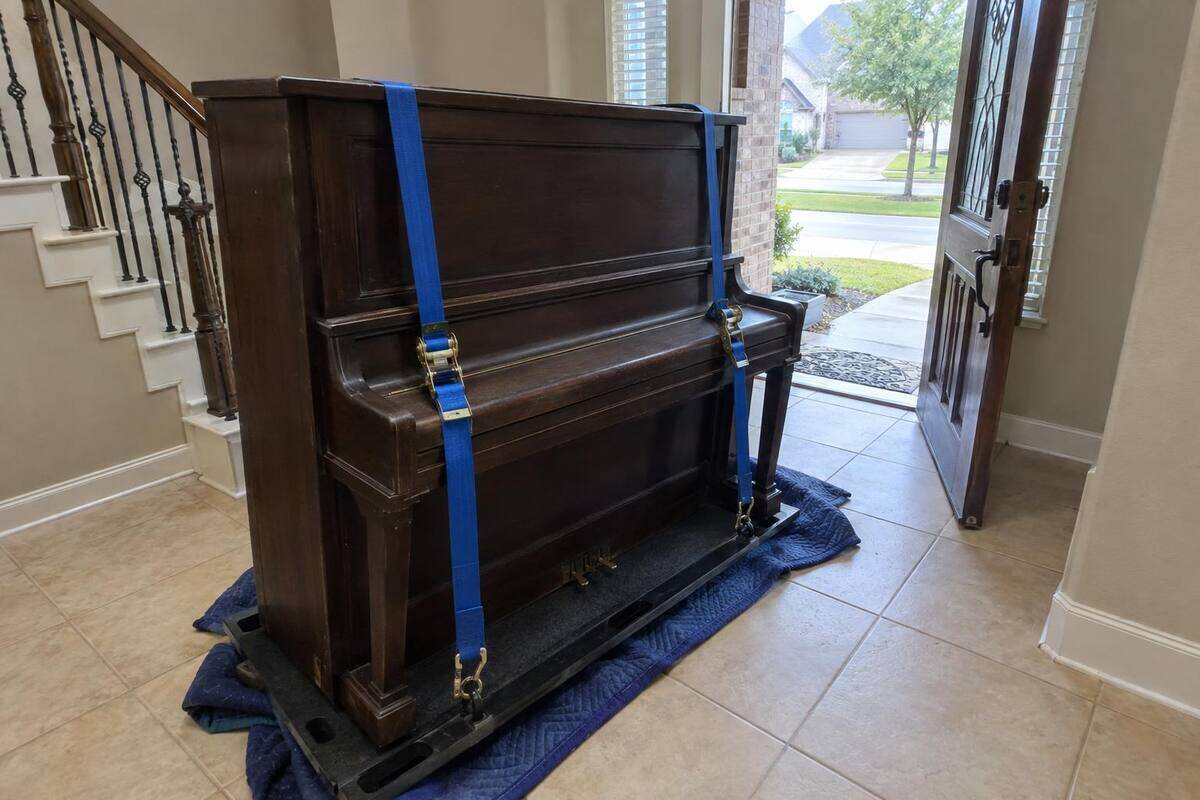 An old upright piano strapped to a padded skid board in a tiled entry hall